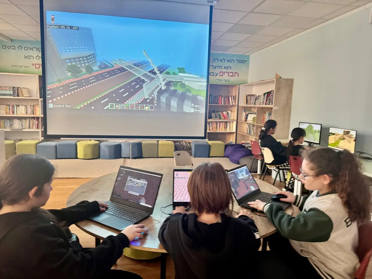 A class building a city in Minecraft on laptops, with their world projected on the big screen